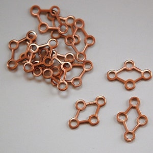 May include: A pile of copper-colored metal connectors, each shaped like a diamond with five holes. There are three individual connectors on a white surface.