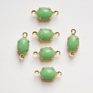 Könnte beinhalten: Sechs ovale, grüne Glasperlen mit goldenen Metallfassungen. Jede Perle hat zwei Schlaufen an beiden Seiten zum Anbringen an Schmuck oder anderen Bastelarbeiten.