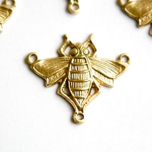 May include: Gold-toned metal bee charm with two jump rings. The bee has detailed wings and a textured body.