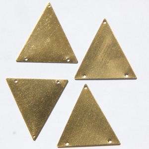 May include: Four brass-coloured triangle connectors, each with three holes. The metal has a slightly aged appearance, with visible surface texture. These components are likely for jewellery making or craft projects.