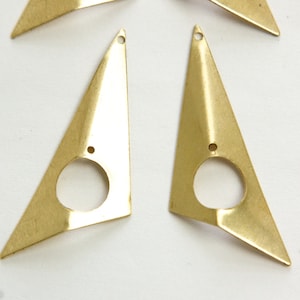 May include: Two gold-colored metal triangle earrings with a circular cutout in the center. The earrings have a slightly irregular shape and a pointed tip.