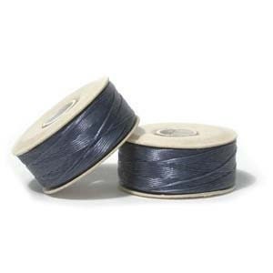 May include: Two spools of dark grey thread, each wound on a white cardboard bobbin.