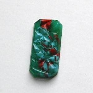 Puede incluir: Un cabujón rectangular de vidrio verde y rojo con un patrón de remolino. El cabujón está cortado en estilo facetado.