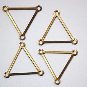 Pode incluir: Quatro formas triangulares de metal dourado com cantos arredondados e pequenos furos em cada canto.