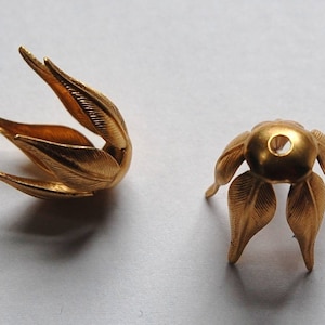 May include: Two gold metal flower-shaped embellishments. One is open and the other is closed. Both have a hole in the center.