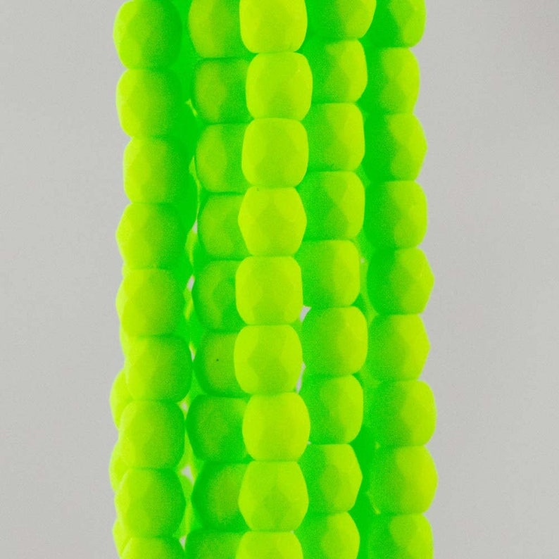 May include: A vertical arrangement of five parallel strands of neon lime green beads. Each bead features a faceted, multi-sided geometric shape with a matte finish. The beads are uniform in size and color, creating a bright, textured appearance.