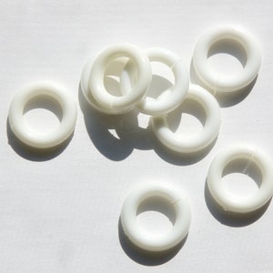 May include: A group of eight white plastic rings, likely used for curtains or other home decor.