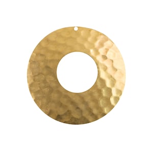 Puede incluir: Un círculo de metal dorado con textura martillada y un agujero en el centro. El círculo tiene un diámetro de aproximadamente 5 cm.