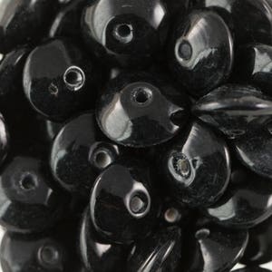 Puede incluir: Primer plano de un montón de cuentas de vidrio negras. Las cuentas son redondas y tienen un pequeño agujero en el centro. Son perfectas para hacer joyas u otros proyectos de manualidades.