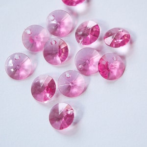 Puede incluir: Una colección de cuentas de cristal rosa con un diseño facetado. Las cuentas son redondas y tienen un agujero en el centro para enhebrar.