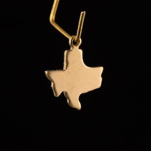 May include: Gold-colored earring featuring a cutout of the state of Texas.