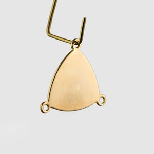 May include: Gold triangle earring finding with three jump rings. The earring finding is a triangle shape with a smooth, shiny surface. The jump rings are attached to the corners of the triangle.