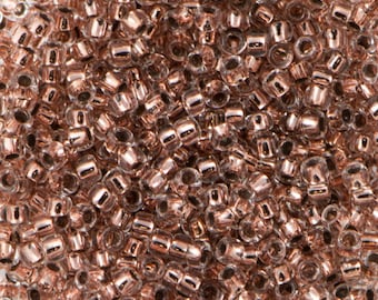 May include: A close-up image of a large quantity of small, round, clear glass beads with a rose gold metallic coating.