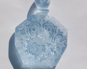 May include: A light blue glass bottle with a decorative etched design. The bottle has a round stopper and a hexagonal body.