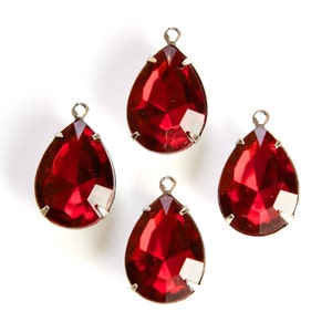 May include: Four red teardrop-shaped glass beads with silver metal settings. The beads are faceted and have a shiny finish.