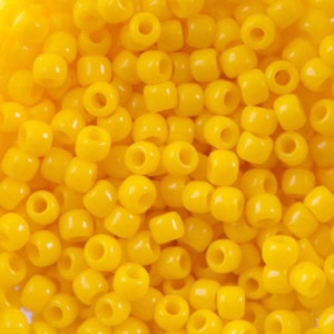 Puede incluir: Primer plano de un montón de pequeñas cuentas amarillas opacas. Las cuentas son cilíndricas con un agujero en el centro. Las cuentas están dispersas, llenando el marco, y son de un color amarillo brillante uniforme.