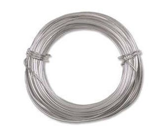 Puede incluir: Una bobina de alambre plateado, bien enrollada y asegurada. El alambre parece fino y flexible, adecuado para manualidades o joyería. La bobina está centrada sobre un fondo blanco liso.