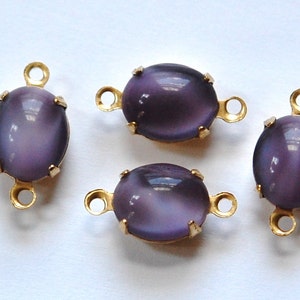 May include: Four oval-shaped, purple cabochon beads with a cat's eye effect. Each bead is set in a gold-colored metal frame with loops for stringing. The beads are a soft, muted purple color.