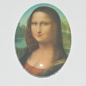 May include: Oval ceramic tile with a printed image of the Mona Lisa, a famous painting by Leonardo da Vinci. The tile features a light blue background with a green landscape and a portrait of the Mona Lisa with a subtle smile.