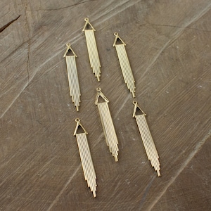 May include: Seven gold-toned metal pendant charms with a geometric design. Each charm features a triangular top and a series of vertical lines.