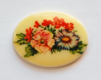 May include: An oval-shaped, cream-colored ceramic tile with a floral design. The design features pink, red, and blue flowers with green leaves.