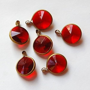 Pode incluir: Seis pingentes de vidro vermelho com engastes de metal dourado. Os pingentes são redondos e têm um design facetado.