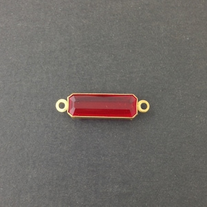 May include: A gold-toned connector with a red rectangular glass stone in the center. The connector has two loops on either side.