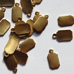 May include: A group of gold-colored metal tags with a hole at the top. The tags are various shapes and sizes, and some have rounded corners.