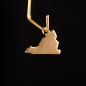 May include: A gold-colored pendant shaped like the state of Virginia. The pendant is hanging from a gold-colored chain.