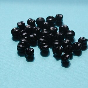 May include: A pile of black twisted glass beads on a blue background.