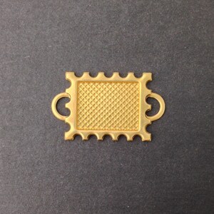 以下が含まれることがあります： 正方形のフレームとダイヤモンドパターンを持つ金色の金属製コネクタ。コネクタには両側に2つのループがあります。