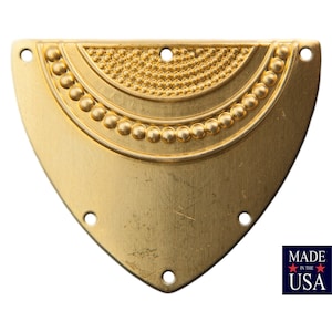 Puede incluir: Un adorno de metal de forma triangular de color dorado con un diseño decorativo de tres círculos concéntricos de cuentas. El adorno tiene cinco agujeros alrededor del borde.