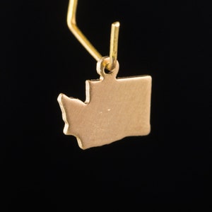 May include: Gold earring featuring a cutout of the state of Washington.