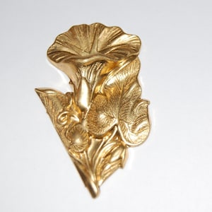 Puede incluir: Un diseño de flor de metal dorado con una flor y hojas estilizadas. El diseño es detallado e intrincado.