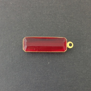 Pode incluir: Um pingente retangular de vidro vermelho com uma moldura de metal dourado e um laço dourado para prender a uma corrente ou cordão.
