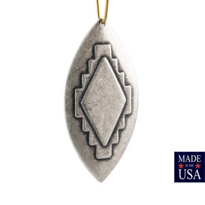 May include: A silver-toned, teardrop-shaped pendant with a geometric design. The pendant features a central diamond shape surrounded by stepped rectangular patterns. A gold-colored loop is at the top for hanging. The image includes a "Made in the USA" label.