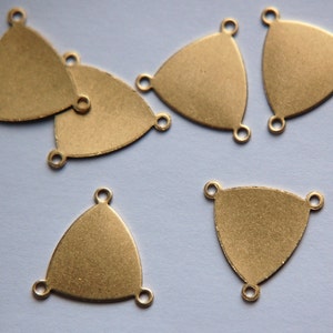 Puede incluir: Cinco abalorios de metal de forma triangular de color dorado con tres agujeros cada uno. Los abalorios están sobre una superficie azul claro.