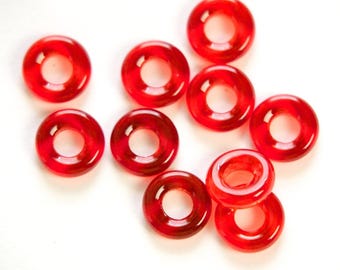 May include: A collection of translucent, red, ring-shaped beads. The beads are scattered on a white background. The beads have a glossy finish and a hole in the centre. These beads are suitable for jewellery making.