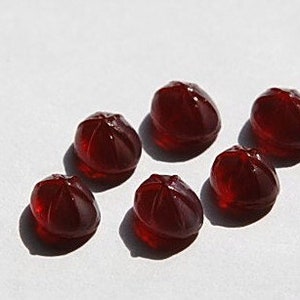 May include: Six dark red, candy-like, dome-shaped objects on a white surface.