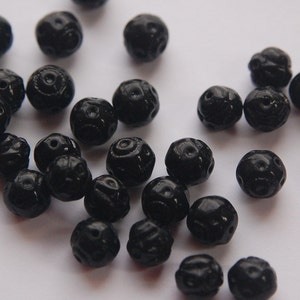 Könnte beinhalten: Eine Sammlung schwarzer, runder Perlen mit aufwendigen Schnitzereien. Die Perlen sind auf einer weißen Oberfläche verstreut.