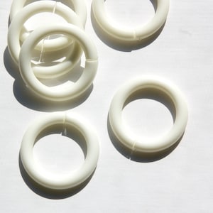 May include: Five white plastic rings, some stacked on top of each other, on a white background.
