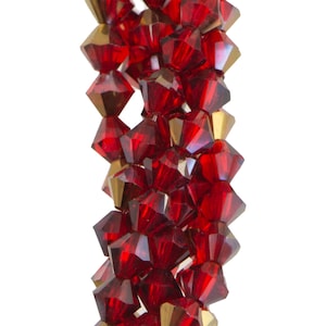 May include: Close-up of a strand of faceted beads. The beads are a deep red colour with gold-coloured accents. The beads are arranged in a vertical line against a white background. The beads have a geometric shape.