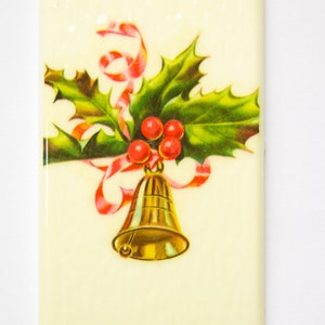 May include: A vintage Christmas card featuring a gold bell with a red ribbon and holly leaves with red berries.