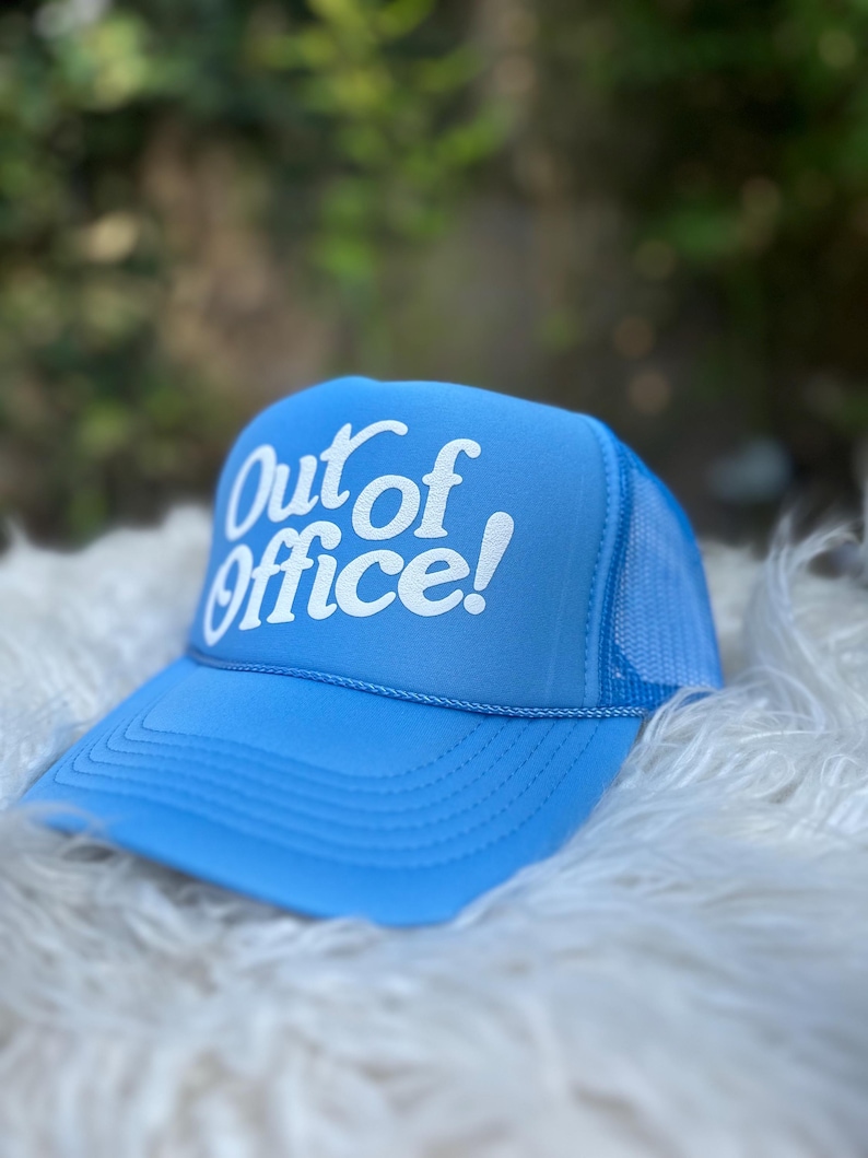 Może przedstawiać: Jasnoniebieska czapka trucker z siateczką z tyłu. Na czapce z przodu widnieje napis "Out of Office!" w kolorze białym.