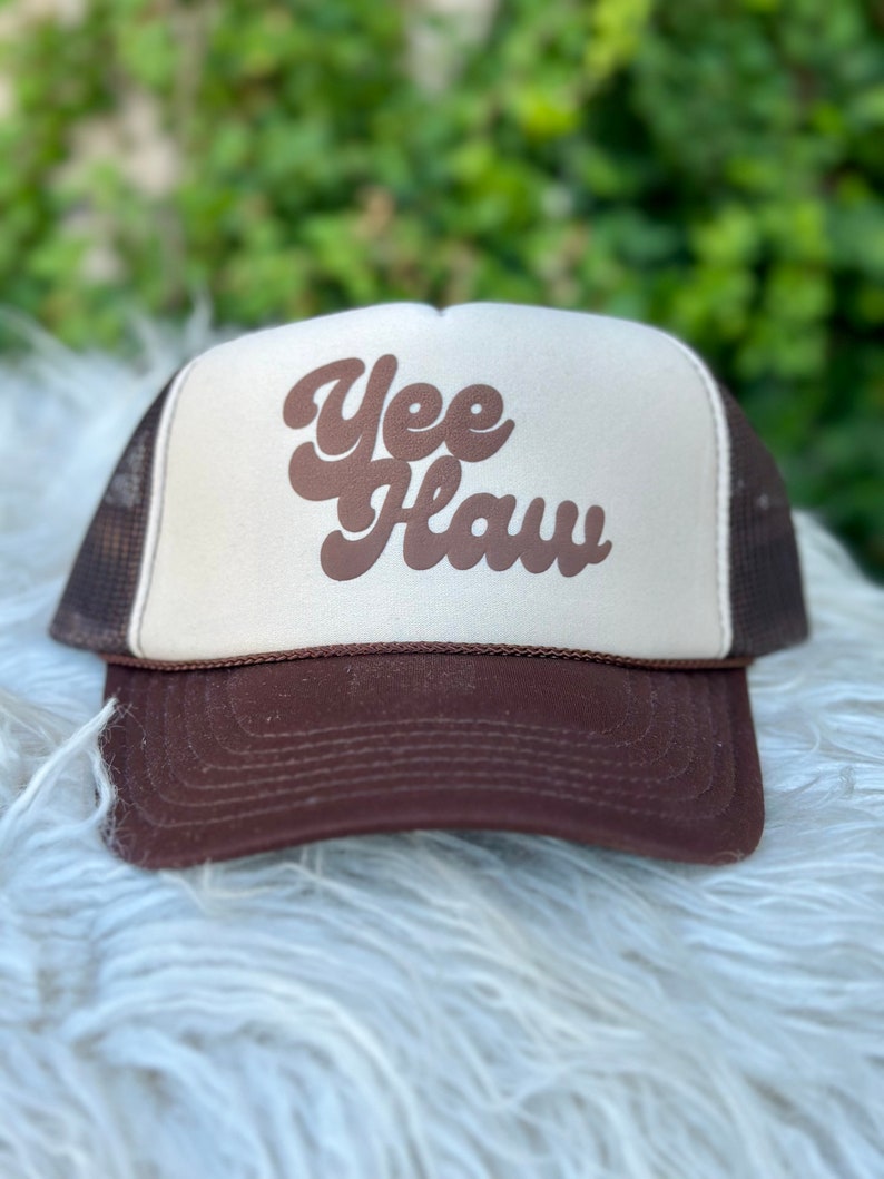 May include: A brown and white trucker hat with a brown "Yee Haw" logo in a retro font.
