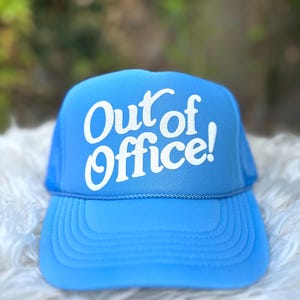 Może przedstawiać: Niebieska czapka trucker z białą siatką i białym nadrukiem "Out of Office!"