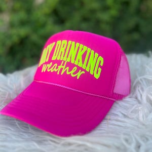 Puede incluir: Gorra de camionero de malla rosa con una inscripci&oacute;n en verde ne&oacute;n "Day Drinking Weather".