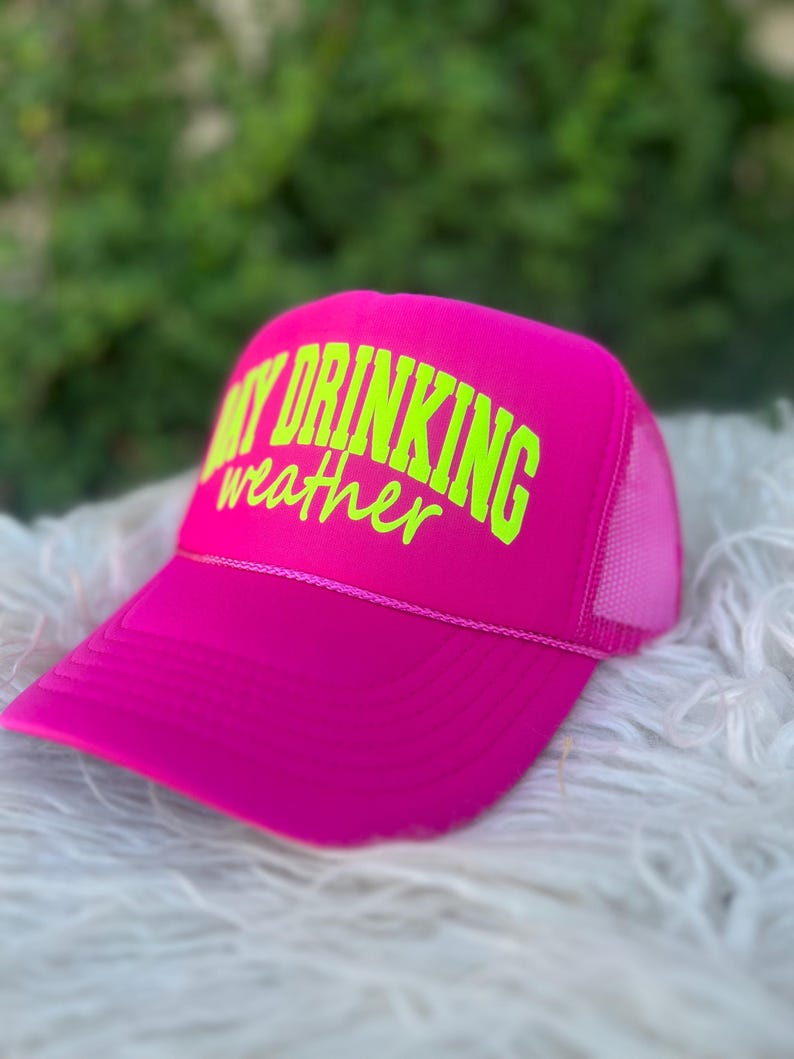 Puede incluir: Gorra de camionero de malla rosa con una inscripci&oacute;n en verde ne&oacute;n "Day Drinking Weather".