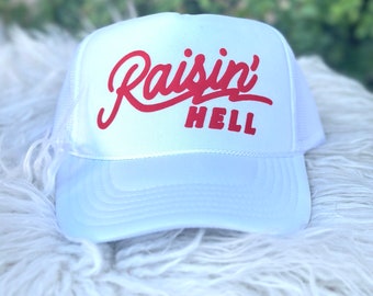 May include: White mesh trucker hat with red embroidered text that says "Raisin' Hell".