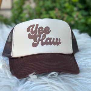 May include: A brown and white trucker hat with the text "Yee Haw" in brown script lettering.